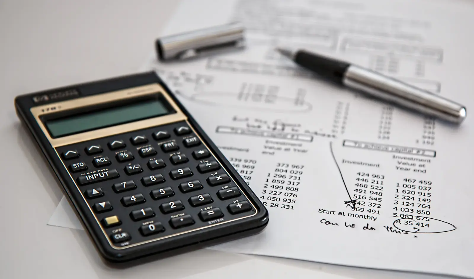 A calculator and pen resting on a printed sheet of investment figures
